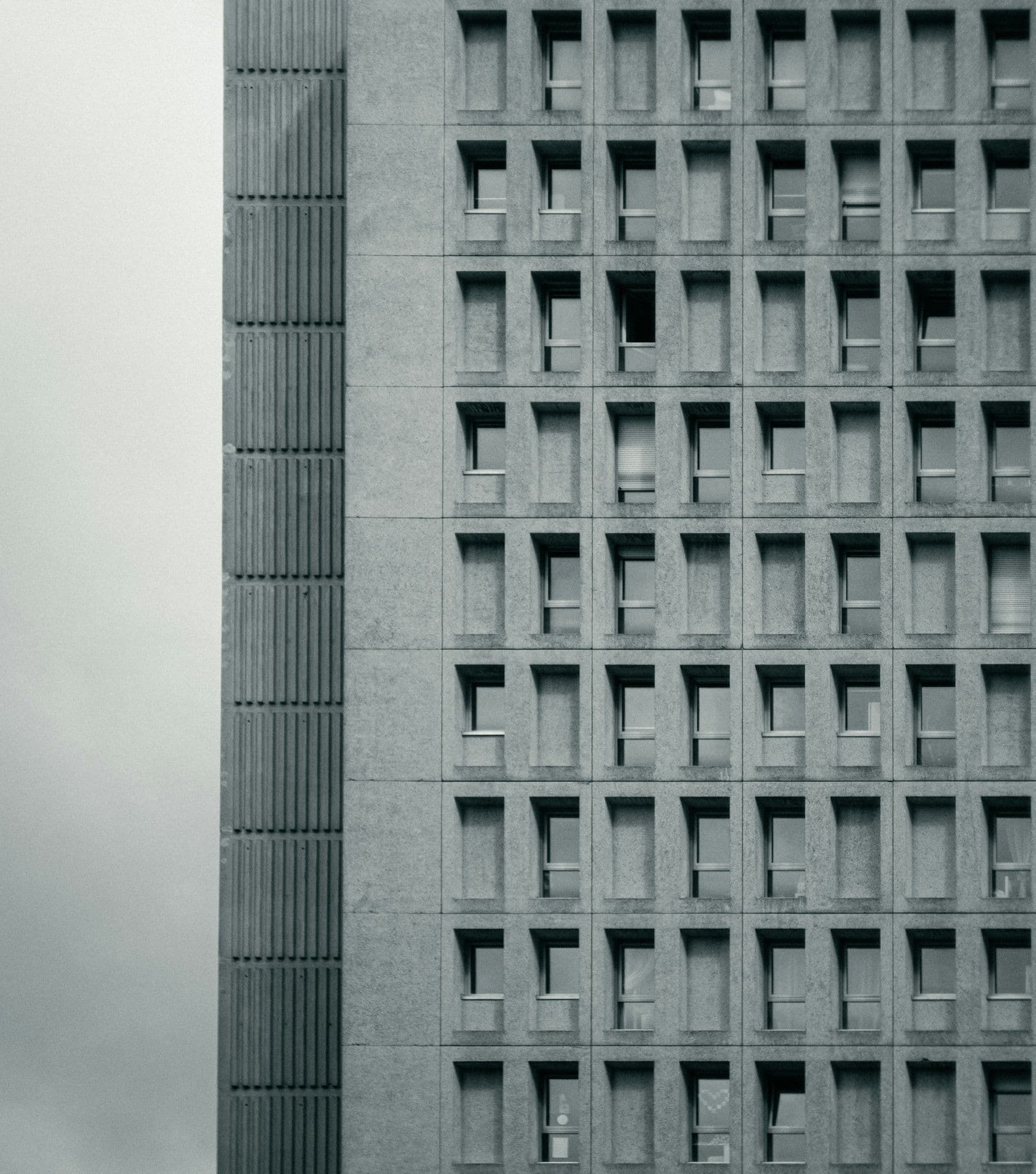 Černobílý detail betonové fasády s pravidelným rastrem oken